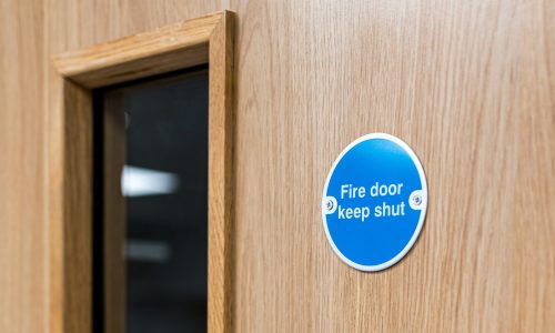Close-up of a typical Fire Door Keep Shut sign seen on an interior door within a British hospital. The firedog prevents any fire or smoke spreading in the building.