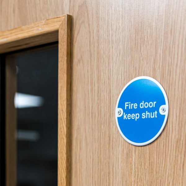 Close-up of a typical Fire Door Keep Shut sign seen on an interior door within a British hospital. The firedog prevents any fire or smoke spreading in the building.